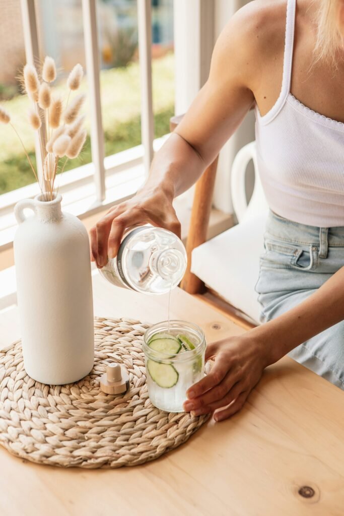 A glass pitcher of room-temperature infused water with fresh cucumber and mint prepared for gentle summer digestion